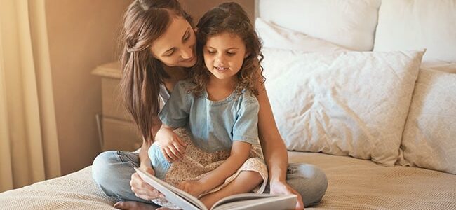 En mamma och dotter sitter och läser en bok tillsammans i sängen.